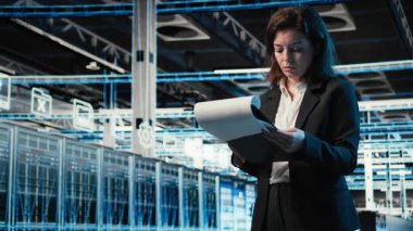 Veri merkezi yönetimi evrakları okuyor, mavi kablo ağ donanım donanımlarını inceliyor. Sunucu çiftliğinde çalışan kadın AR altyapı görselleştirmesi ile çevrili belgeleri analiz ediyor. Kamera A