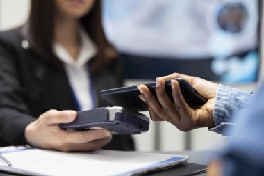 Nakitsiz tıbbi ödeme için akıllı telefonu kullanan bir hasta, klinik resepsiyonisti olarak kart okuyucusuyla işlem yapıyor. Siyah şahıs hastane ücretini ödüyor, cep telefonu cihazını ses cihazına bağlıyor..