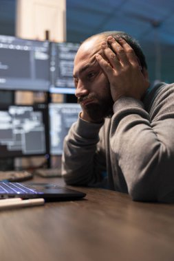 Aşırı çalışan programcı zor kodlama oturumunda avuçlarında dinleniyor. Erkek geliştirici, dizüstü bilgisayardaki karmaşık verileri tükenmiş ifadeyle analiz eder, programlama stresi ve teknik olarak