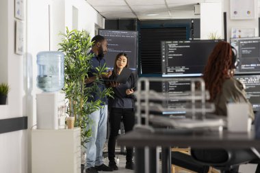 Profesyonel kodculardan oluşan çeşitli takımlar programlama çözümlerini tartışıyor ve dizüstü bilgisayardaki kaynak kodlarını gözden geçiriyorlar. Afrikalı Amerikalı ve Asyalı geliştiriciler takım çalışması ve dijital teknoloji büyümesini destekliyor.