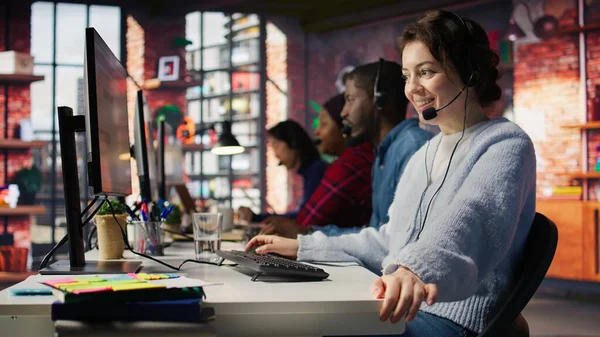 Dost canlısı çağrı merkezi çalışanı, ses kulaklığıyla konuşuyor, müşterilere ofisinde yardım ediyor. Müşteri destek operatörü telefon görüşmesi sırasında müşterilerle iletişim kuruyor. Kamera B, kapat.