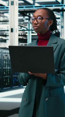 Veritabanlarını, laptop 'ı ve kadın teknisyenleri destekli gerçeklik depolama platformlarıyla veri merkezine doğru yürüyorlar. Bulut bilgisayarı, VFX örtüsü ve sunucuda çalışan Afrikalı Amerikalı kadın.