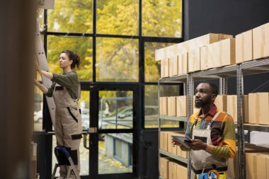 Afrika kökenli Amerikalı personel küçük bir depoda paketleri ve paletleri inceliyor, e-ticaret sevkiyat operasyonlarını destekliyor ve perakende malları için kalite kontrolü sağlıyor. Toptan kargo ürünleri..