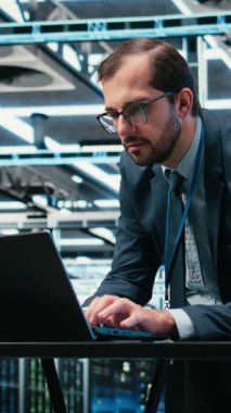 Laptop klavyesine yazıp, yazılım kullanarak kaynak optimizasyonu yapan dikey video merkezi yönetimi. Donanım süper bilgisayarlarını, kamera A 'yı güncellemek için dizüstü bilgisayar programı kullanan sunucu çiftliği bilişim uzmanı