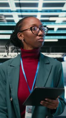 Dikey video mühendisi veri merkezinde, hata kayıtlarını ve hata ayıklama sistemlerini izlemek için tablet ve AR teknolojisini kullanarak yürüyor. Sunucu merkezindeki Afro-Amerikalı kadın mavi kablo şebekesinde tarama yapıyor.