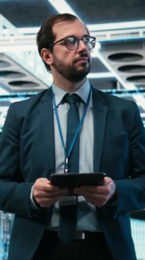 Dik Veri Merkezi bilgisayar bilimcisi tablet uygulamasını kullanarak çevrimiçi platformlara güç veren ekipmanları yönetiyor. Adam sunucu odasına giriyor, dokunmatik ekranı kullanarak dijital depolama sistemlerinin bakımını yapıyor.