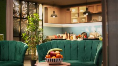 Modern ev içinde bir kase meyve. Mutfak alanına bağlı oturma odası sergilenmiyor. Şık kanepe ve ahşap masa, dekoratif meyveler rahat bir ev ortamı yaratır..