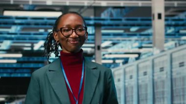 Gülümseyen veri merkezinin portresi. Kadın mühendis, internet hizmetlerine yardımcı olan ekipman yöneticiliği. Sunucu odasındaki neşeli Afro-Amerikalı kadın dijital depolama sistemleri için yapıldı, kamera B