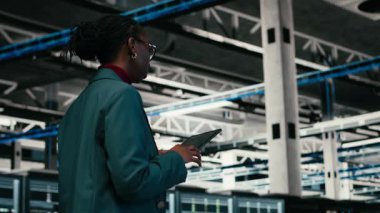 Kod yazma, tablet ve kadın programcı veri merkezinde yürüyor, yazılım yamaları derliyor. Programlama betiği çalıştırılıyor, aygıt uygulaması ve sunucu merkezinde Afrikalı Amerikalı kadın, kamera B