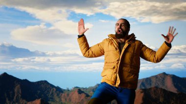 Mutlu tırmanışçı seviniyor ve kollarını gökyüzüne doğru açarken kişisel başarı ve zaferin memnuniyetini hissediyor. Göz kamaştırıcı panoramik manzara. Kamera B.