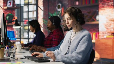 Kulaklık takan ajanlardan oluşan çağrı merkezi ekibi modern iş istasyonunda müşterilere birden fazla monitörle yardımcı oluyor. Müşteri desteğini, iletişim ve hizmet verimliliğini, kamera A 'yı vurguluyorlar.