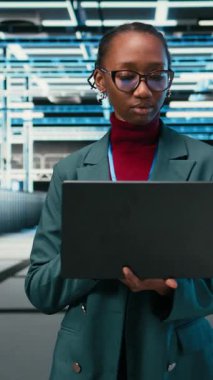 Veritabanı veri merkezinde yürüyen dikey video teknisyeni, veritabanı depolama platformlarını yönetmek için laptop ve artırılmış gerçeklik kullanıyor. Bulut hesaplama sunucu çiftliğinde çalışan Afrikalı Amerikalı kadın, VFX