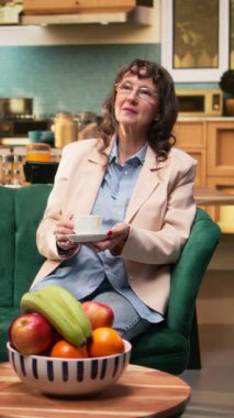 Dikey Video sunucusu erkek ve kadın kanepede kahve fincanlarıyla hayal kuruyor ve rahatlıyor, yaşlılık bağımsızlığı ve arkadaşlıktan memnun hissediyorlar. Çiftler boş zamanlarında dinleniyorlar, dinleniyorlar..