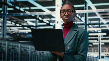 İzleme sistemleri, dizüstü bilgisayarı ve AR simülasyon veri merkezinde yürüyen kadın programcı. Optimizasyon, VFX birleşimi ve sunucu merkezinde not defteri, kamera B kullanarak Afrikalı Amerikalı kadın.