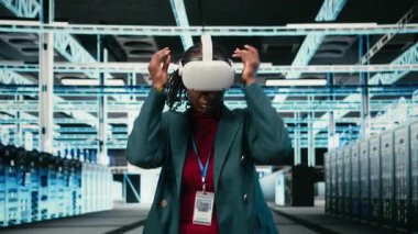 Veri Merkezi kadın mühendisi VR gözlüklerini takıp dişli donanımı optimize ediyor. Sanal gerçekliği kullanarak sunucu odasında Afrikalı Amerikalı bir kadın var ve ana bilgisayarları, kamera A 'yı geliştirmek için zoom el hareketleri yapıyor.