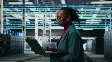 Bilgisayar yazılımı kullanarak kaynak optimizasyonu yapan mutlu veri merkezi sistem yöneticisinin portresi. Sunucu merkezinde gülümseyen genç bir çalışan bilgisayarla IT altyapısını, kamera A 'yı güncelliyor.