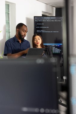 Erkek ve kadın müteahhitler teknoloji ofisinde işbirliği yaparak dizüstü bilgisayardaki yazılım verilerini gözden geçirirler. Çeşitli kodlayıcılar HTML betiklerini birlikte analiz ederek, takım çalışması yoluyla web sitesinin işlevselliğini geliştirir.