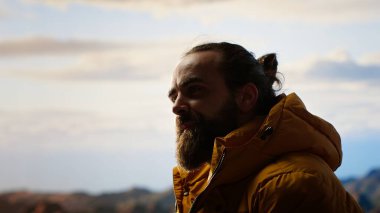 Zirveye çıktıktan sonra dağda gevşeyen muzaffer yürüyüşçü, kişisel başarılarıyla gurur duyuyor. Genç adam kayalarda oturuyor ve huzurlu ortamın tadını çıkarıyor. Kamera B.