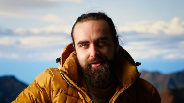 Kaşif, bir dağ zirvesine ulaşmanın heyecanını kucaklıyor ve dinleniyor, temiz havayı ve panoramik güzelliği hissediyor. Yürüyüşçü heyecanlı ve yorgun, kendini geliştirme ve hedefleriyle gurur duyuyor. Kamera B.