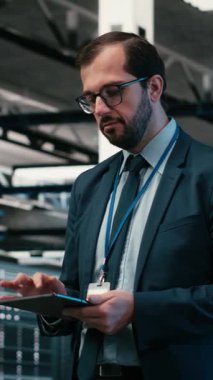 Dik Veri Merkezi bilgisayar bilimcisi tablet uygulamasını kullanarak çevrimiçi platformlara güç veren ekipmanları yönetiyor. Adam sunucu odasına giriyor, dokunmatik ekranı kullanarak dijital depolama sistemlerinin bakımını yapıyor.