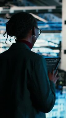 Vertical video yazılım geliştiricisi hata ayıklamak için tablet ve AR teknolojisini kullanarak veri merkezinde yürüyor. Sunucu çiftliği bilişim uzmanı mavi kablo ağ ekipmanı üzerinde teşhis çalıştırıyor