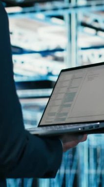 Bilgisayar kullanarak çevrimiçi platformlara güç veren ekipmanları yöneten veri merkezi mühendisinin dikey videosu. Sunucu merkezi çalışanı programlama betiği kullanarak dijital depolama sistemlerini kontrol ediyor