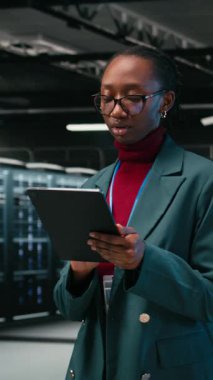 Hata ayıklama sistemleri, tablet ve kadın mühendis AR teknolojisini kullanarak veri merkezine giriyor. Tanılama çalıştırılıyor, mavi kablo örgüsü ve sunucuda Afrikalı Amerikalı bir kadın var.