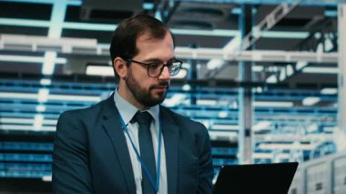 Veri Merkezi Sistem Yöneticisi, gelecekten güvenlikli şirket ağı için dizüstü bilgisayar kullanıyor. Sunucu odasında çalışan adam siber güvenlik önlemlerini artırıyor. Not defteri cihazı, kamera B