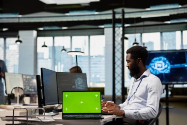 Tecrit edilmiş ekran dizüstü bilgisayarında yapay zeka ölçümlerini inceleyen, performans gösterge panellerini izleyen yeni teknoloji firması yöneticisi. Afrika kökenli Amerikalı bir adam nöral ağları ayarlıyor. Model defterindeki araçları kullanarak.