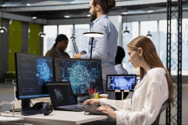 Ofisteki kadın bilgisayar bilimci yapay zekaya birden fazla aygıt üzerinden görevler yürütmesi, ekranlardaki ilerlemeyi izlemesi için güveniyor. Stajyerlik yapan genç teknoloji işçisi yapay zeka geliştirmek için sinirsel ağlar kullanıyor.