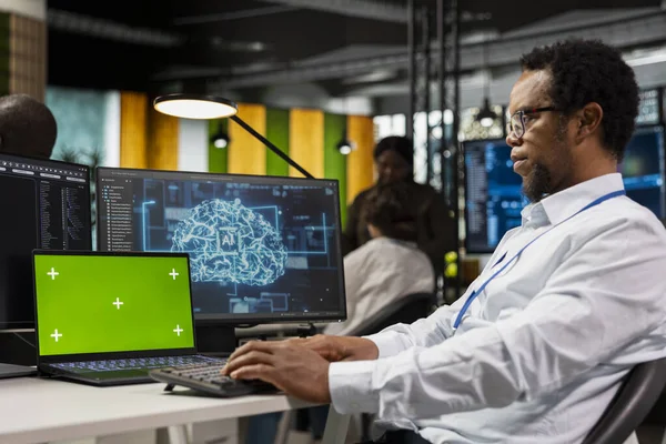 Başlangıç çalışma alanında AI algoritmaları çalıştıran sistem yöneticisi tarafından kullanılan yeşil ekran laptop. Afrika kökenli Amerikalı bir adam yapay zeka kullanıyor. Derinlemesine öğrenme platformu kullanıyor.