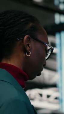 Veri merkezinde kaynak optimizasyonu yapan dikey video yazma kodu, tablet uygulaması ve programcı. Yükseltme ekipmanı, programlama metni ve sunucuda yürüyen Afrikalı Amerikalı kadın.