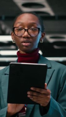 Hata ayıklama sistemleri, tablet ve kadın mühendis AR teknolojisini kullanarak veri merkezine giriyor. Tanılama çalıştırılıyor, mavi kablo örgüsü ve sunucuda Afrikalı Amerikalı bir kadın var.