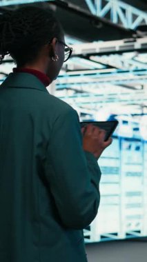 Dikey video yazma kodu, tablet ve kadın programcı veri merkezinde yürüyor, yazılım yamaları derliyor. Programlama betiği, aygıt uygulaması ve sunucu merkezinde Afrikalı Amerikalı kadın çalıştırılıyor