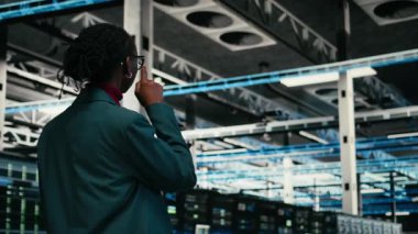 Tablet uygulaması kullanılarak kaynak optimizasyonu için veri merkezi programcısı kod yazıyor. Afrika kökenli Amerikalı kadın sunucu merkezine giriyor. Ekipman geliştirmek için programlama metni kullanıyor. Kamera A.