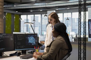 Kıdemli mühendis Dev 'e derin öğrenme algoritmalarını otomatik görevlere nasıl ayarlayacağını gösteriyor. Teknik ekip lideri stajyere kod optimizasyonu için yapay zeka kullanmasını öğretiyor.