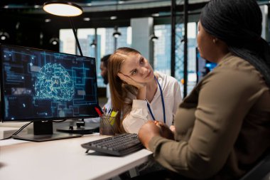 Sad young girl at work receives comforting support from caring AI tech startup coworker. Distressed junior developer gets help from senior colleague listening to her and giving advice