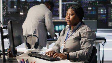 Veri merkezi geliştirici kodlaması PC 'de, yapay zeka süper bilgisayarları için yazılım güncellemeleri yapıyor, saate bakıyor. Sunucu çiftliği bilişim uzmanı yapay zeka ve kamera A kullanarak altyapıyı optimize ediyor.