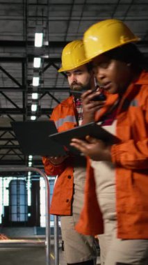 Dikey Görüntü Mühendisi. Metalik iskeleti denetleyen sert şapkalı. Mühendislik fabrikası, ağır sanayi. Üretim salonu bünyesindeki büyük ölçekli makine ve çelik çalışmaları üretim sürecini ön plana çıkarıyor.