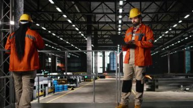 Endüstri uzmanı, ağır ekipmanları denetliyor, dizüstü bilgisayar kullanıyor, fabrika üretiyor. Depodaki ağır makineleri, metal işçiliğini ve üretim hatlarını izleyen adam..