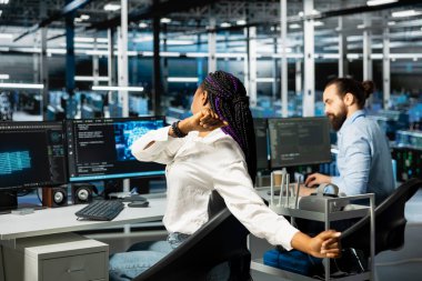 Veri Merkezi kadın mühendisi masa başında uzun saatler çalıştıktan sonra oturma yorgunluğuyla savaşmak için geriliyor. Sunucu merkezindeki Afrikalı Amerikalı kadın yanlış duruşu düzeltiyor, rahatsızlığı hafifletiyor