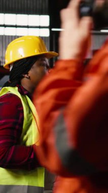 Dikey Video Kadın Mühendisi, üretim salonu boyunca endüstriyel işletim istasyonlarını tabletle denetliyor. Depo tesisinde ağır endüstriyel metaller var. Kıvılcımlar saçan mühendislik fabrikası