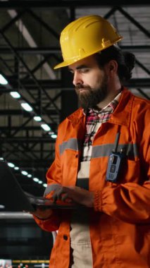 Dikey Görüntü Mühendisi. Metalik iskeleti denetleyen sert şapkalı. Mühendislik fabrikası, ağır sanayi. Üretim salonu bünyesindeki büyük ölçekli makine ve çelik çalışmaları üretim sürecini ön plana çıkarıyor.