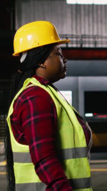 Dikey Video Afrikalı Amerikan mühendisi, ağır endüstri teftişi, üretim salonu, büyük ölçekli üretim deposundaki metal işleri ve ağır makineleri denetleyen kadın. Sanayi alanı