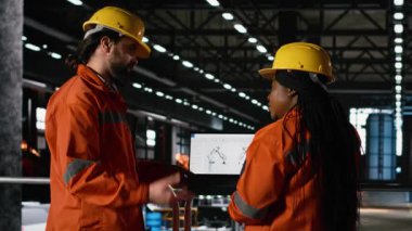 Profesyonel ekip, ağır sanayi fabrikasında dizüstü bilgisayardaki robot kol yazılımını inceliyor, ileri üretim hattı operasyonları için özerk robotik özelliklere sahip yüksek teknoloji mühendislik fabrikası. Ağır makineler.