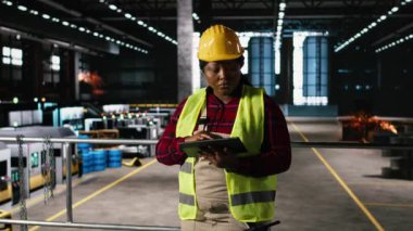 Portre kadın, siyah mühendis, ekipman ve fabrika deposunu değerlendiriyor. Mekanik sistemler ve endüstriyel teknoloji sürekli üretimi sağlarken çelik kirişler tepemizde uzanıyor..