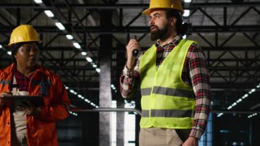 Erkek, endüstriyel operasyonları telsizle koordine ederek, verimli ağır sanayi imalat faaliyetleri için iş arkadaşları arasında iki yönlü telsiz iletişimi sağlıyor..