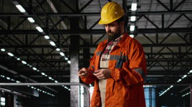 Kasketli ve güvenlik gözlüklü profesyonel mühendisin portresi ağır bir sanayi deposunda makineleri denetliyor. Büyük metal kirişleri ve çelik işçiliği olan endüstriyel mühendislik tesisi..