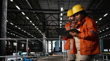 Metalik iskeleti, mühendislik fabrikasında ve ağır sanayide inceleyen sağlam şapkalı bir mühendis. Üretim salonu bünyesindeki büyük ölçekli makine ve çelik çalışmaları üretim sürecini ön plana çıkarıyor.