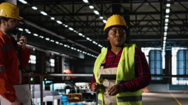 Afrikalı Amerikalı kadın, mühendislik fabrikası, şapka, makine performansını kontrol ediyor. Ağır sanayi depolama tesisi içindeki atölye ile üretim hattını denetleyen işçiler.